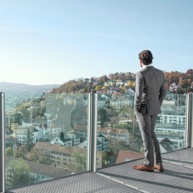 Man looks at a city from a glass balcony 