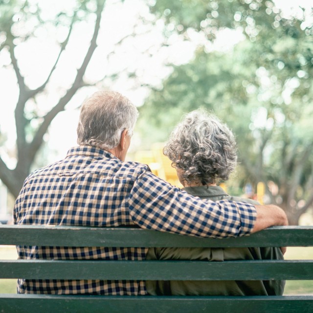Älteres Ehepaar sitzt auf Bank und blickt in die Weite