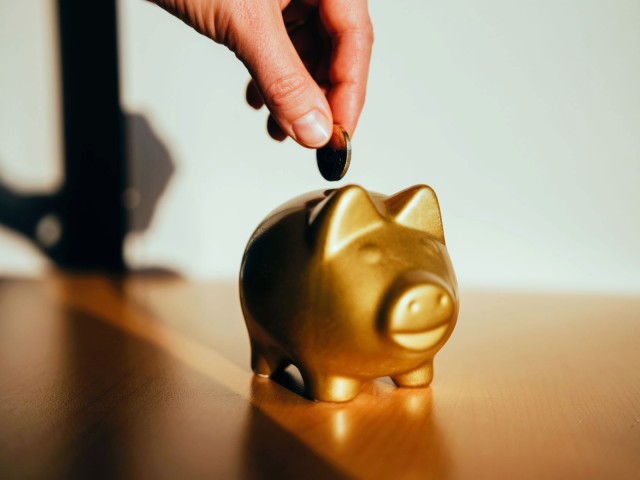 A hand puts a coin into a golden piggy bank