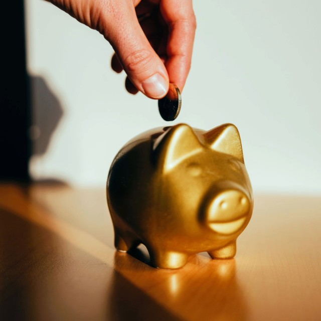 A hand puts a coin into a golden piggy bank