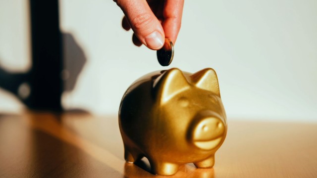 A hand puts a coin into a golden piggy bank