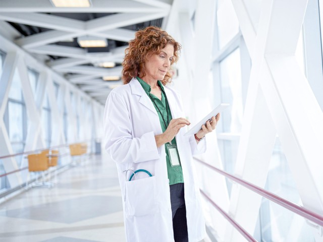 Doctor stands in a glass corridor and holds a tablet in her hand