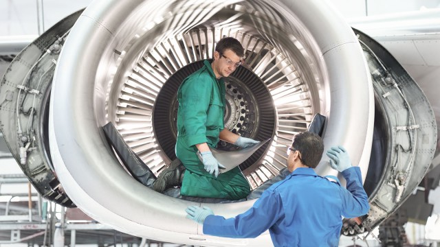 Ein Bauarbeiter kniet in einer Flugzeugturbine und spricht mit Kollegen