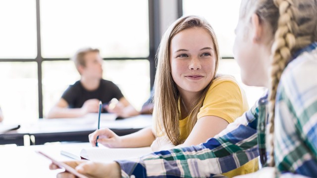 Zwei Schülerinnen sitzen an einem Tisch und lächeln sich an