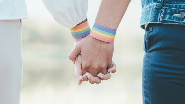 Zwei Personen halten sich an den Händen und beide tragen Regenbogen Armbänder
