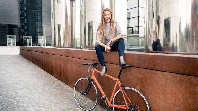 Frau sitzt auf Mauer, Fahrrad steht vor ihr