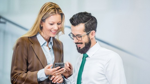 Zwei Kollegen unterhalten sich und schauen auf ein Smartphone