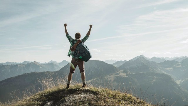 Mann steht triumphierend auf dem Gipfel eines Berges