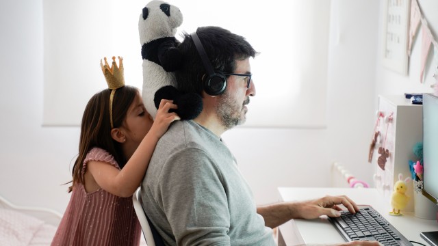 Ein Mann sitzt arbeitend am Schreibtisch und seine Tochter schaut dabei zu