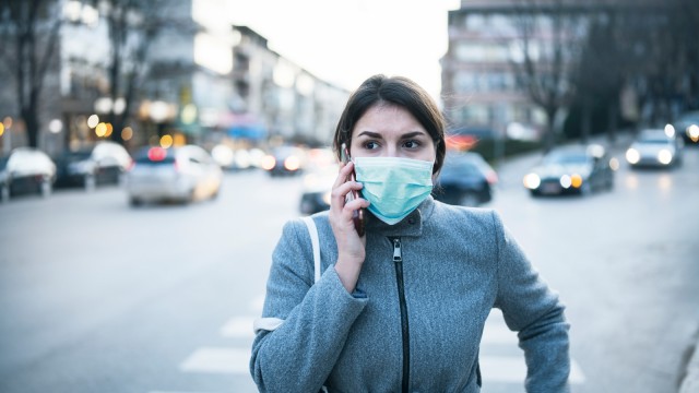 Eine junge Frau mit Mundschutz geht über eeine Straße in einer Metropole