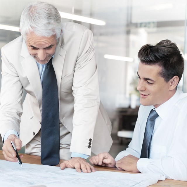 Zwei M&auml;nner die an einem Tisch sitzen und etwas besprechen