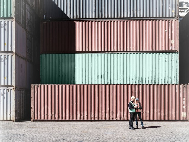 Zwei Personen mit Helm, die vor Containern stehen