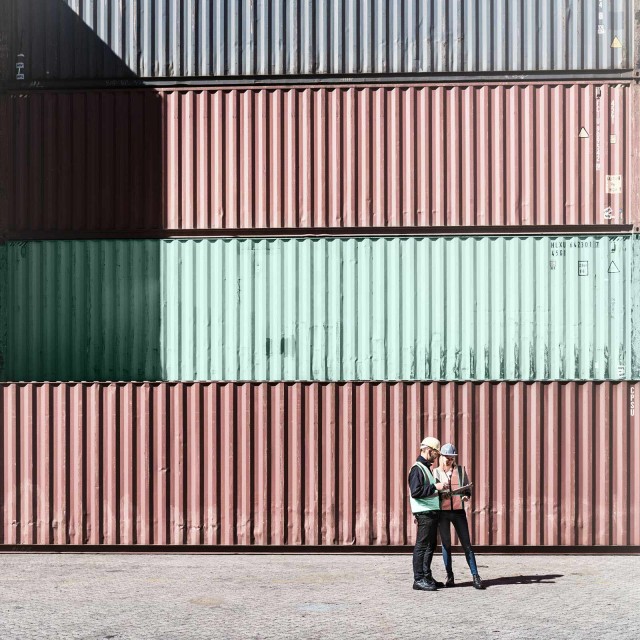 Zwei Personen mit Helm, die vor Containern stehen