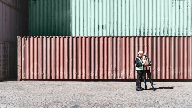 Zwei Personen mit Helm, die vor Containern stehen