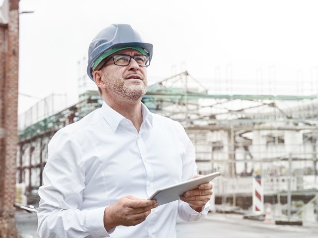 Mann mit Helm und Notebook auf Baustelle: Die LBBW versteht sich als Partner ihrer Geschäftskunden