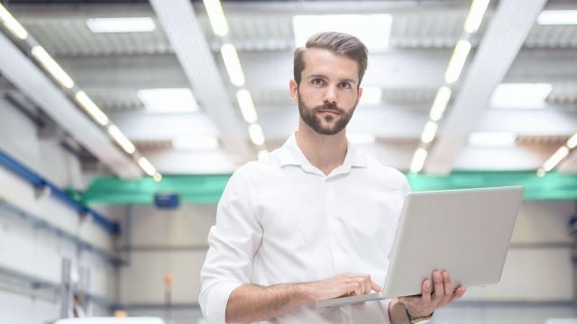 Mann hält Laptop in einer Fabrikhalle 