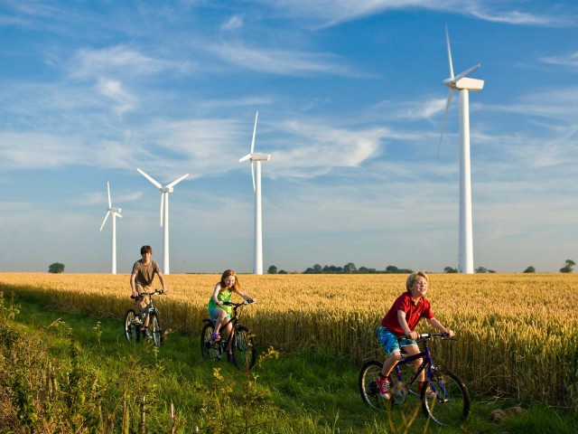 Children riding a bike are passing by a field with windmills