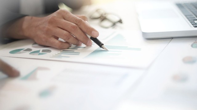 Hand with pen controls graphics on desk: Cash Management at LBBW 