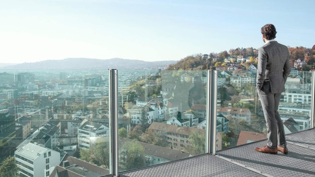 Mann schaut von gläsernem Balkon auf eine Stadt 