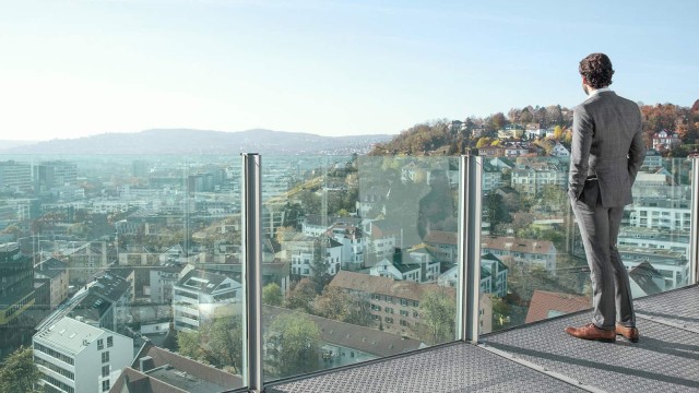 Man looks at a city from a glass balcony 