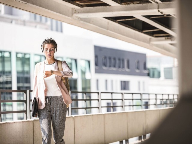 Young businesswoman walks in the parking garage and looks at her watch
