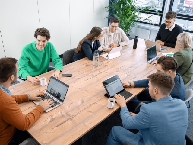 Personen arbeiten an einem gro&szlig;en Konferenztisch mit Laptops und Tablets.