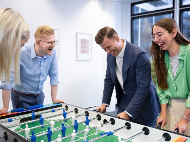 Junge Personen spielen Tischkicker in einem B&uuml;roraum und lachen.