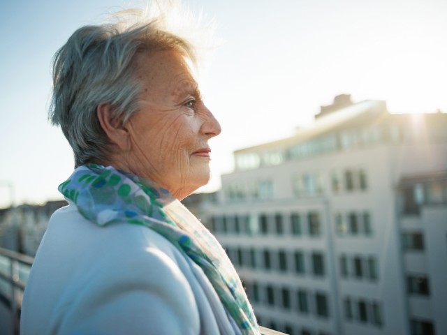 Ältere Dame steht auf Dachterrasse
