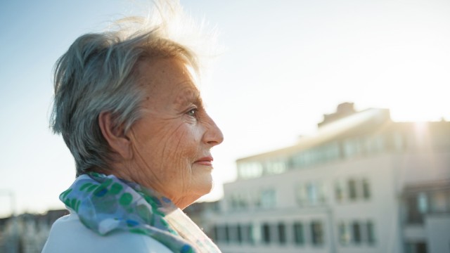 Ältere Dame steht auf Dachterrasse