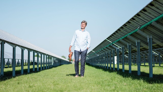 Mann läuft barfuß zwischen Solarpanelen über eine Wiese