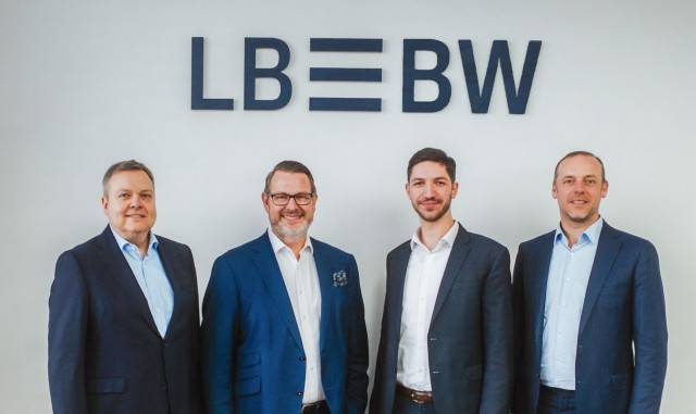 Vier Männer lächelnd vor dem LBBW Logo