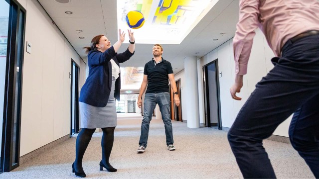 Drei Menschen spielen im Büroflur Volleyball