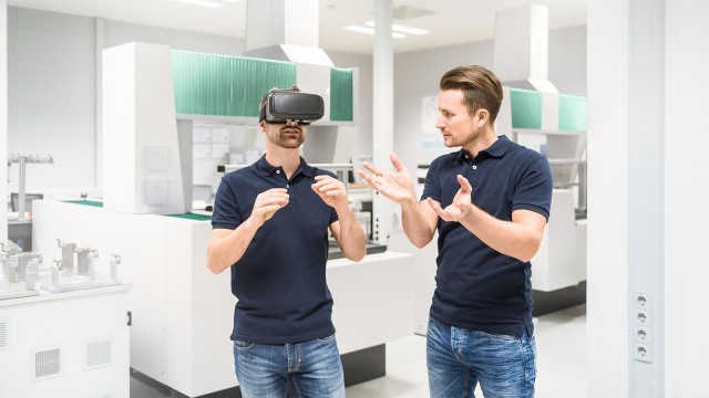 Zwei junge Männer, von denen einer eine Virtual-Reality-Brille trägt 