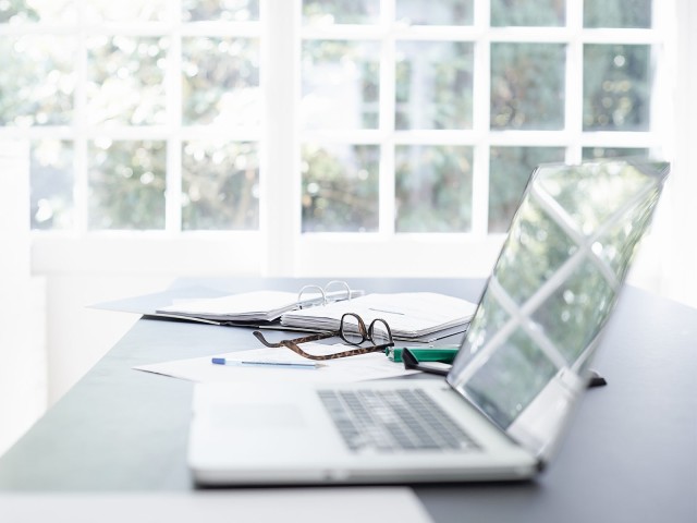 Aufgeklappter Laptop liegt neben Brille auf einem Tisch 