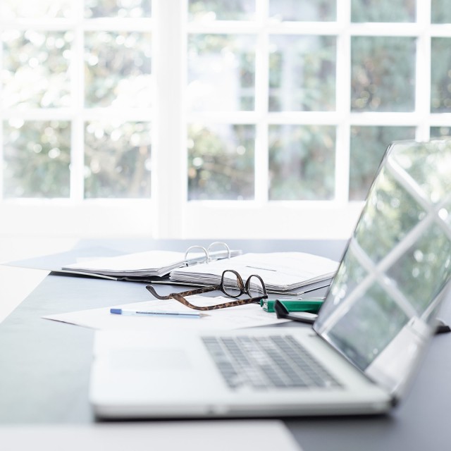 Aufgeklappter Laptop liegt neben Brille auf einem Tisch 