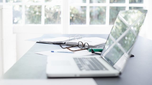 Aufgeklappter Laptop liegt neben Brille auf einem Tisch 