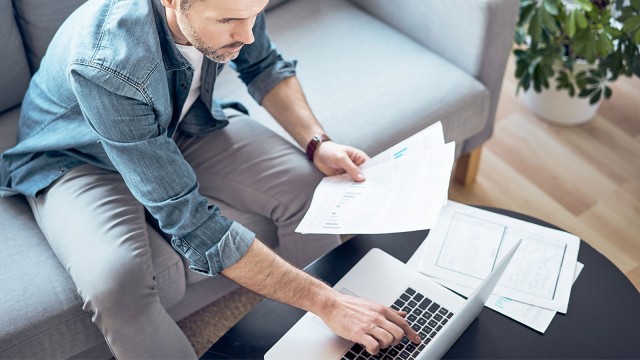 Mann in seinem Wohnzimmer bei der Finanzplanung mit Unterlagen und Laptop