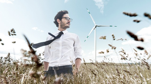 Mann mit Brille und Krawatte steht im Feld vor Windrädern