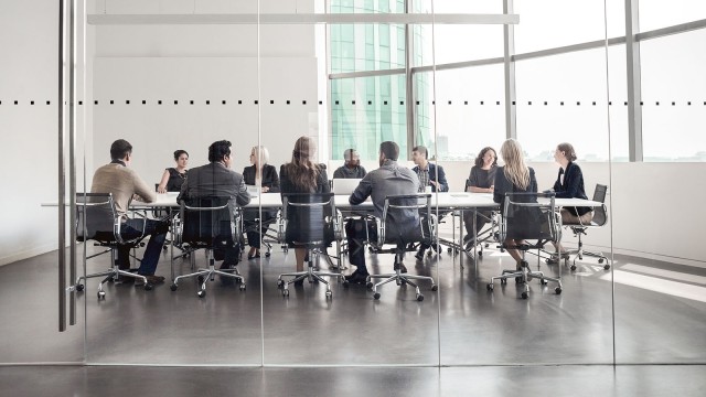 Personen im Meeting am Tisch hinter einer Glasscheibe 