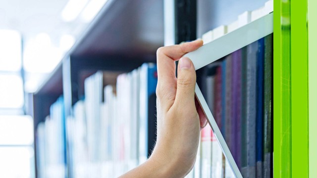 Hand zieht Tablet aus Bücherregal 