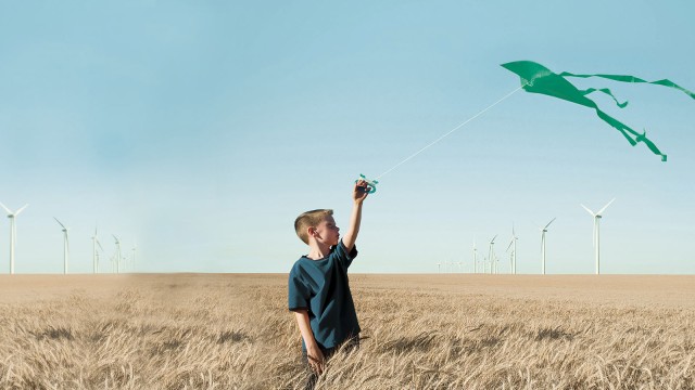 Junge lässt Drachen steigen, im Hintergrund eine Reihe von Windrädern 