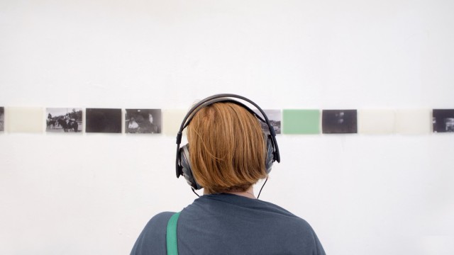 Frau mit Kopfhörern schaut Kunstwerke an Wand an