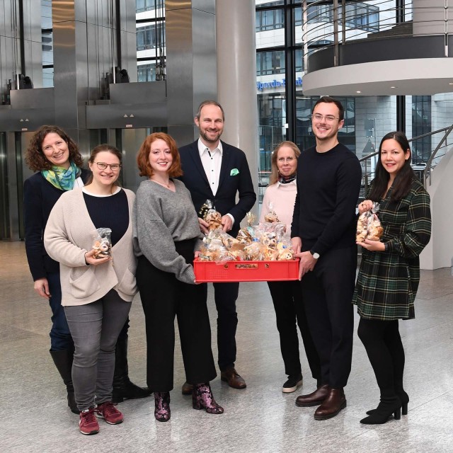 Sozial Aktion in der LBBW, Mitarbeitende stehen mit selbstgebackenen Plätzchen vor Weihnachtsbaum