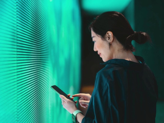 Junge Frau mit einem Smartphone vor LED Panel