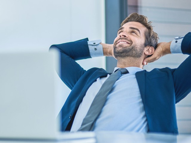 Ein Mann sitzt gemütlich zurückgelehnt am Arbeitsplatz
