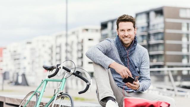 Geschäftsmann in der Stadt und hört Nachrichten mit Kopfhörer und Smartphone