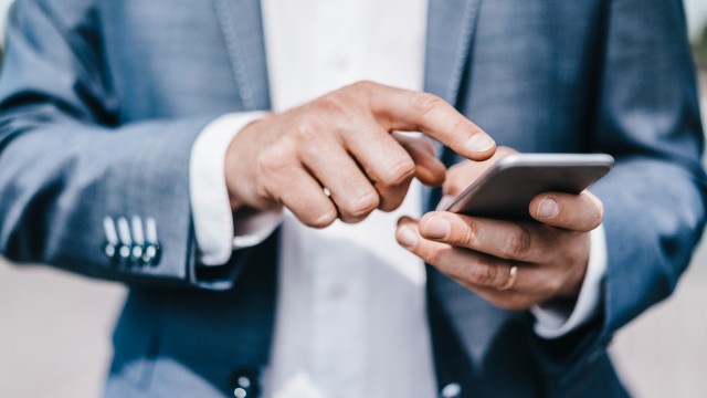 Close-Up der Hände eines Mannes in Anzug, der ein Smartphone bedient