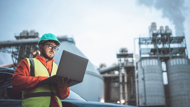 Arbeiter mit Helm und Laptop vor Anlage