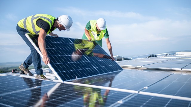 Zwei Ingenieure installieren Sonnenkollektoren auf einem Dach