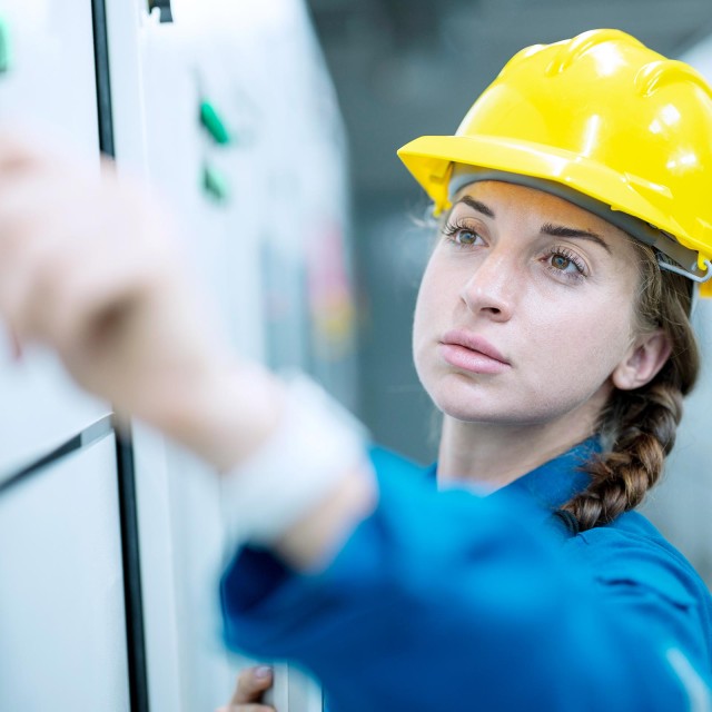 Frau mit gelbem Helm zeichnet etwas an eine Wand